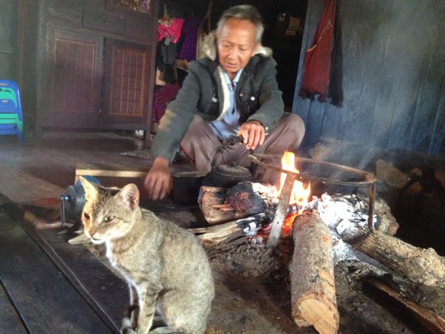 Amaung's father roasting tea on the fire, top cat looks on